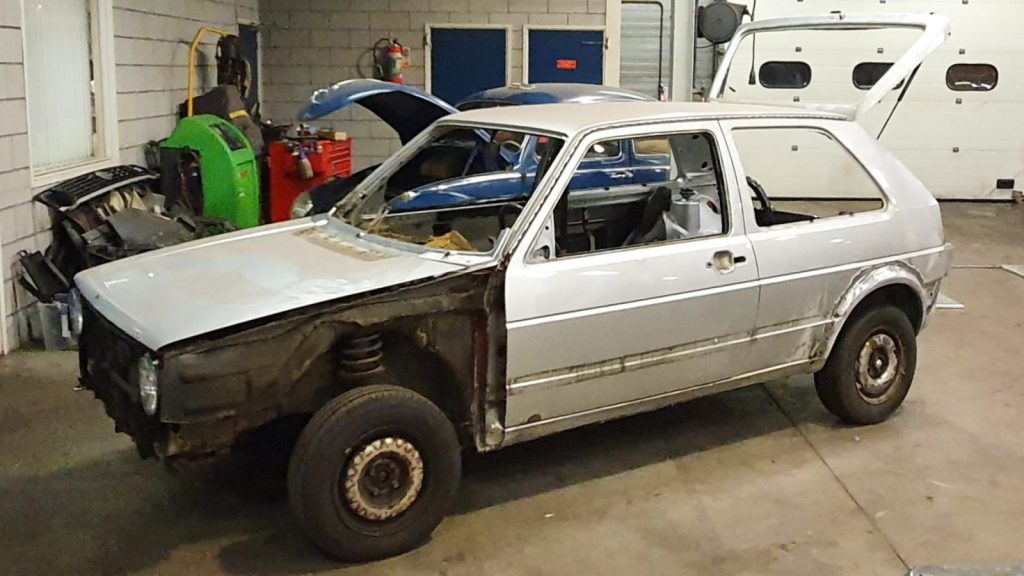 Afbeelding van een VW Golf Mk2 in zilvergrijs metallic in een garage werkplaats, waarbij de auto deels is gedemonteerd tbv de restauratie.